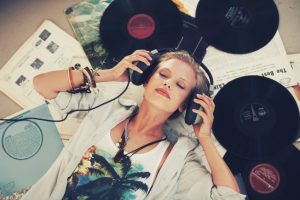 A young woman listening to music while lying on her back and surrounded by records