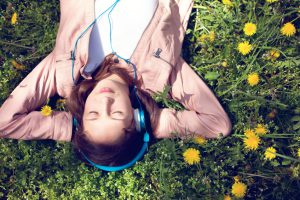 Teenage girl lying on back in the grass with hands behind head.She listens to music with eyes closed.